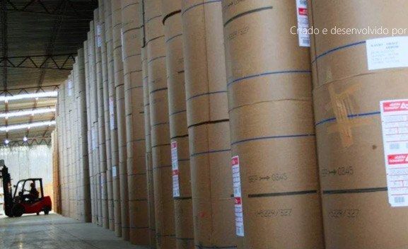 Armazém com bobinas de papel empilhadas e empilhadeira em operação