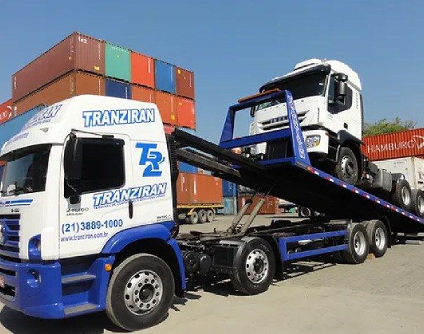 Caminhão plataforma da Tranziran transportando veículo no pátio de contêineres